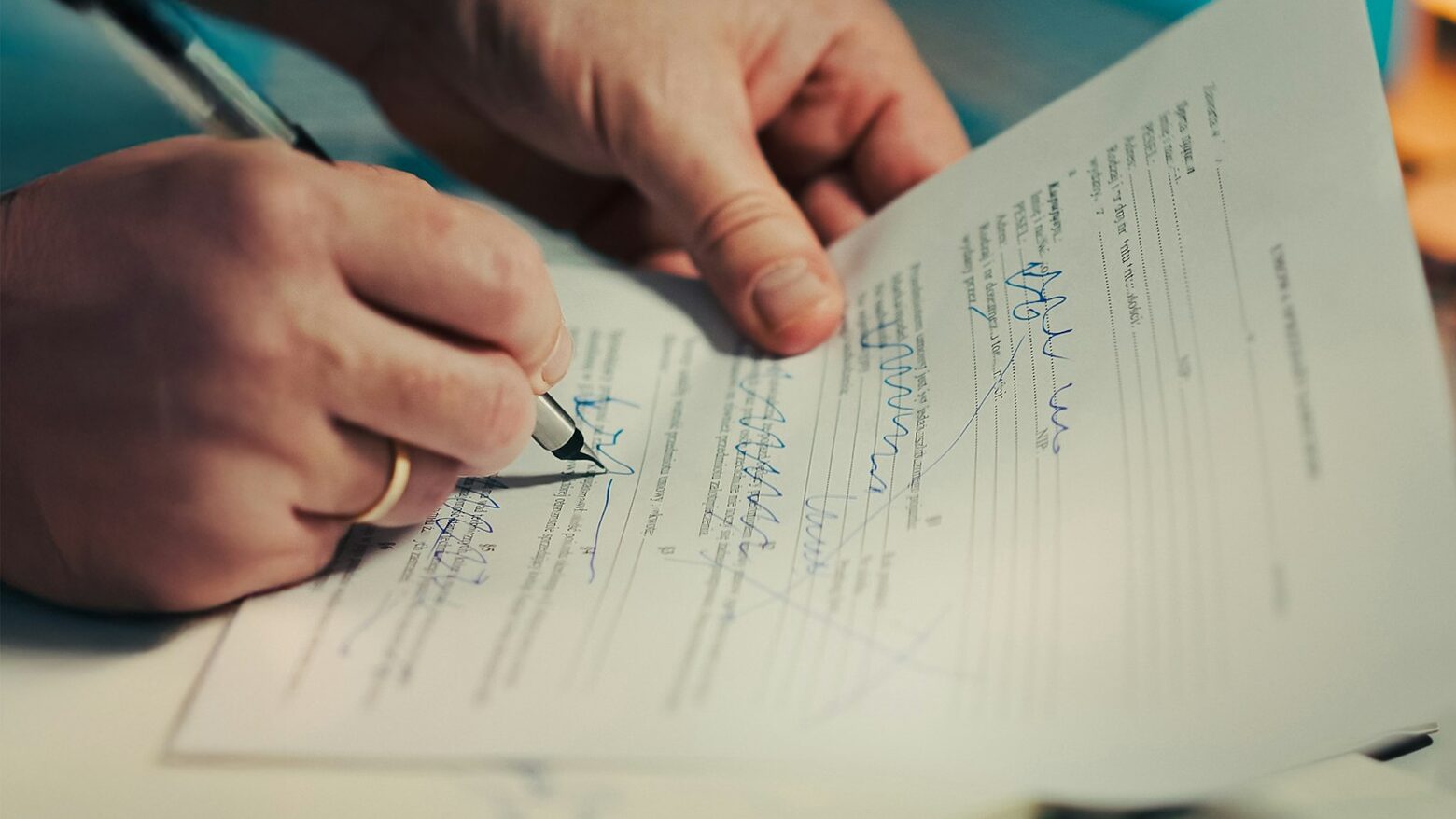 A person signing a paper form with a pen