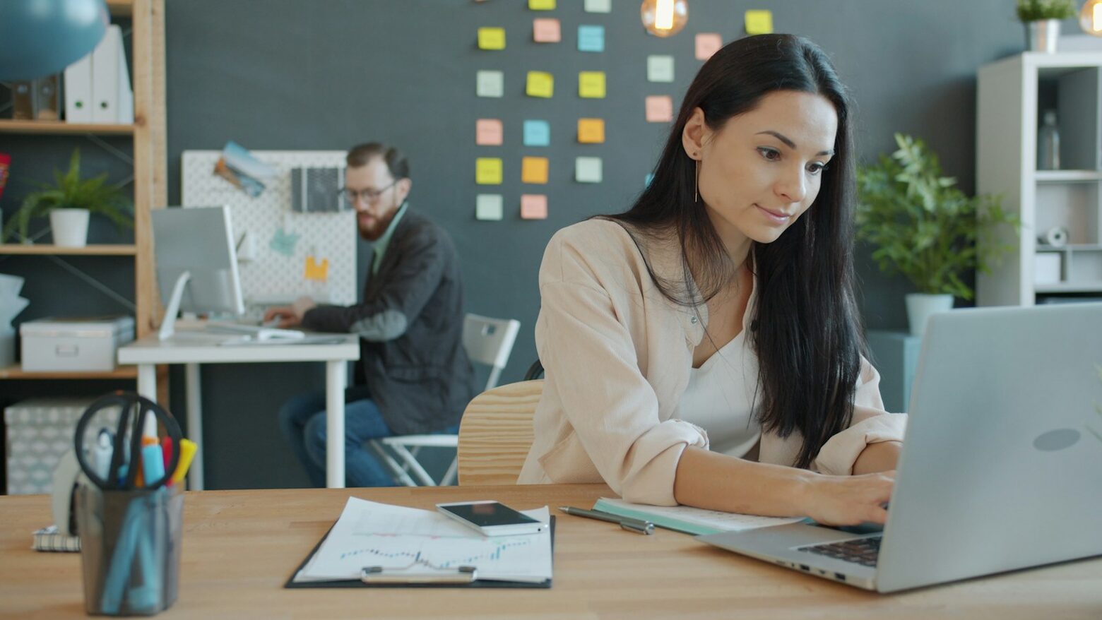A woman working on a laptop at a desk with paperwork
